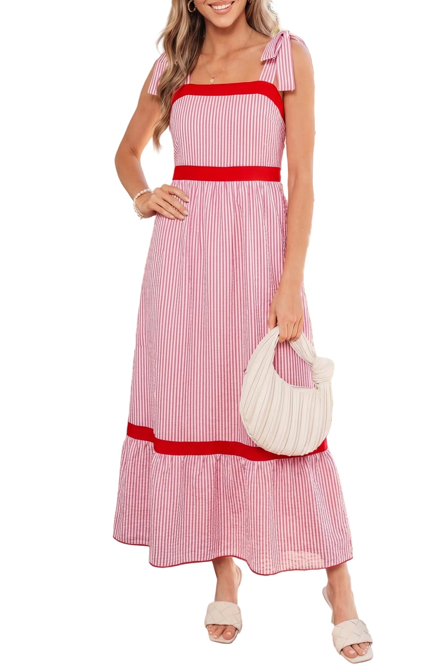 Woman wearing a pink and red striped dress with a white handbag, standing outdoors.
