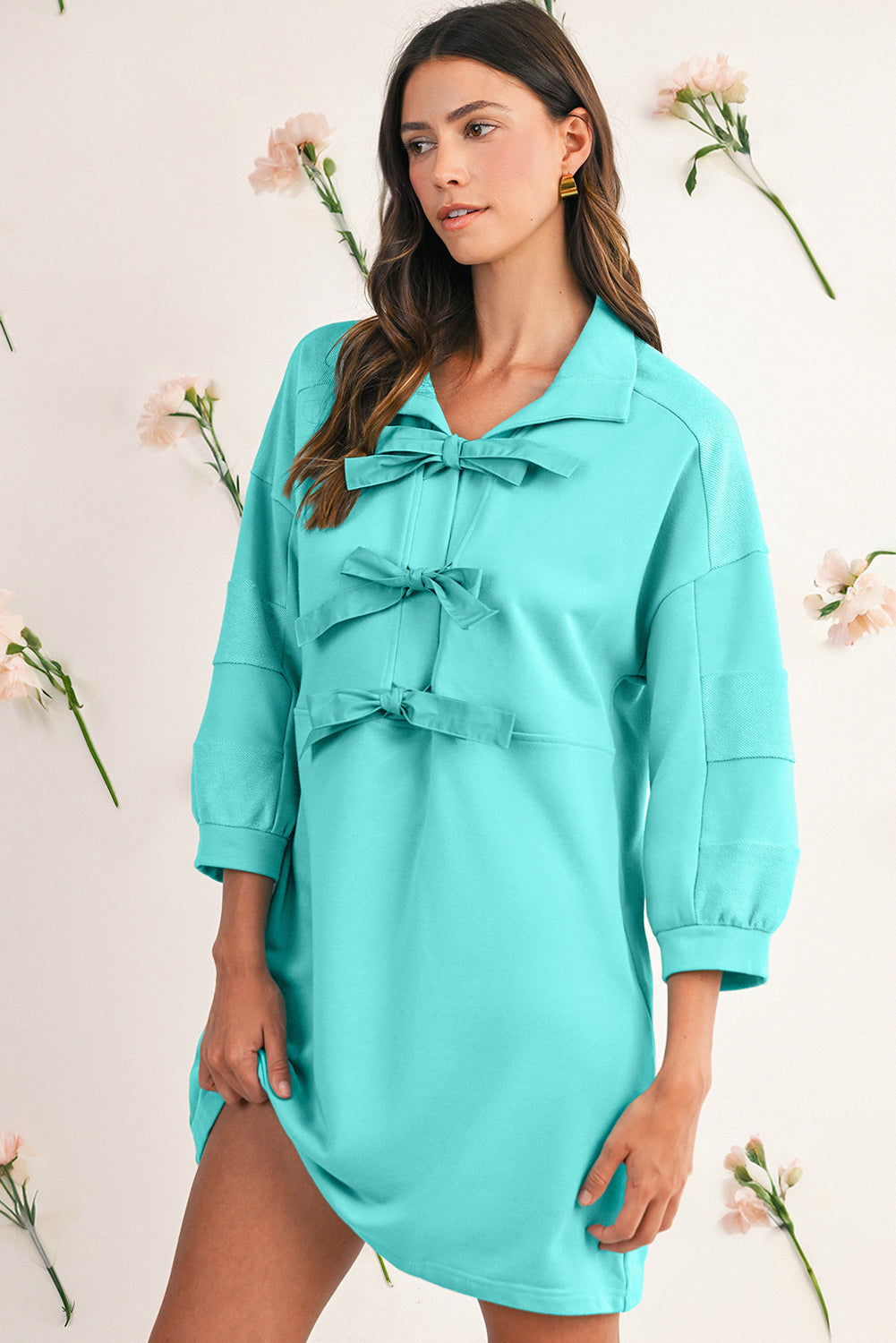 Woman wearing a turquoise dress with floral decorations in the background