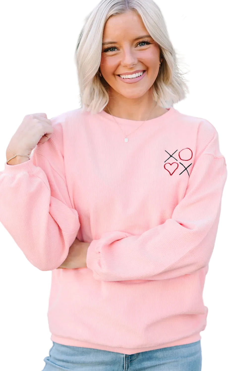 Woman wearing a pink sweatshirt with a heart and cross design, standing outdoors.