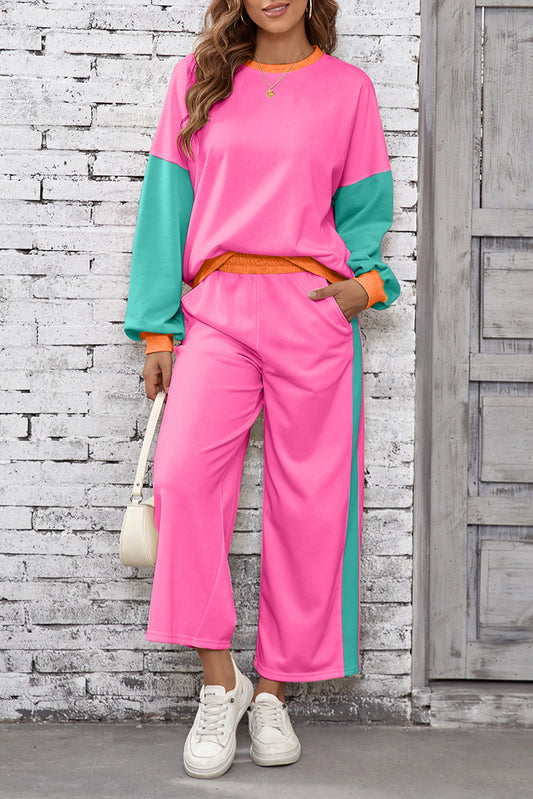 Woman wearing a pink and green color-blocked outfit against a brick wall.