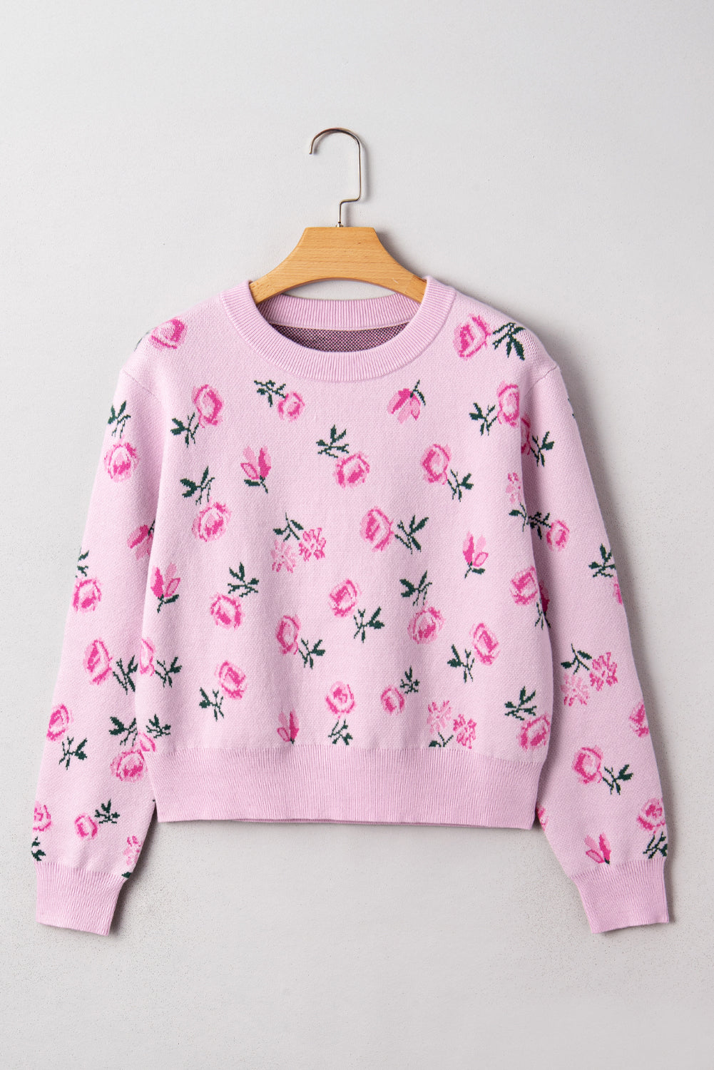 Pink sweatshirt with floral patterns on a wooden hanger against a light gray background