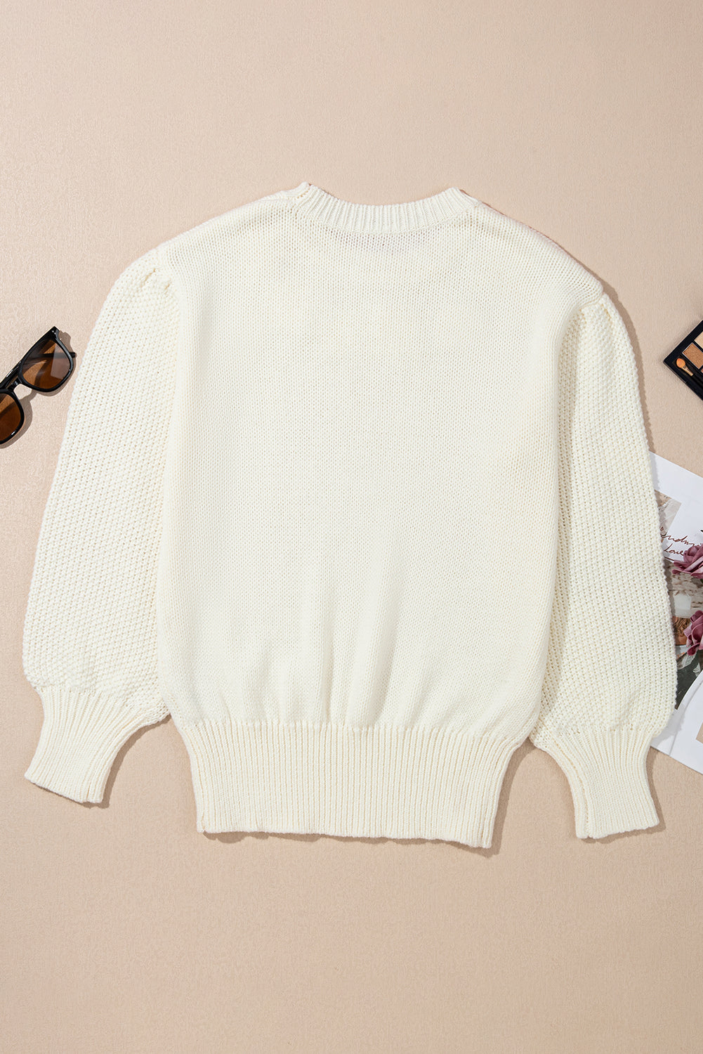 White sweater on a beige background with sunglasses and a magazine.