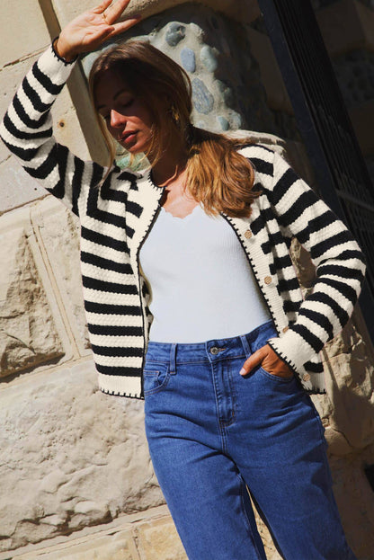 Person wearing a black and white striped cardigan, light blue top, and blue jeans outdoors.