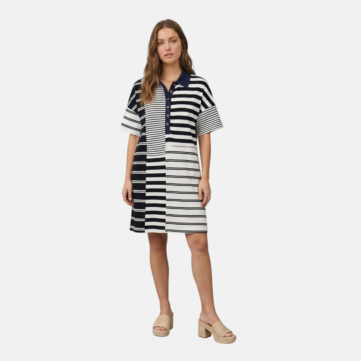 A woman wearing a short-sleeve polo-style mini dress featuring a mixed-stripe pattern in navy and white. The dress has a navy blue collar, a button-down placket, and alternating panels of thick and thin horizontal stripes. She is wearing woven platform slides and a gold chain necklace.
