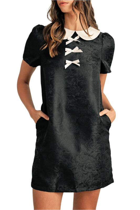 Black floral mini dress with patchwork and puff sleeves. Featuring a charming bow detail on the neckline.