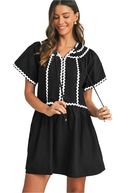 Women wearing a black mini dress with bell sleeves and white ric rac details.