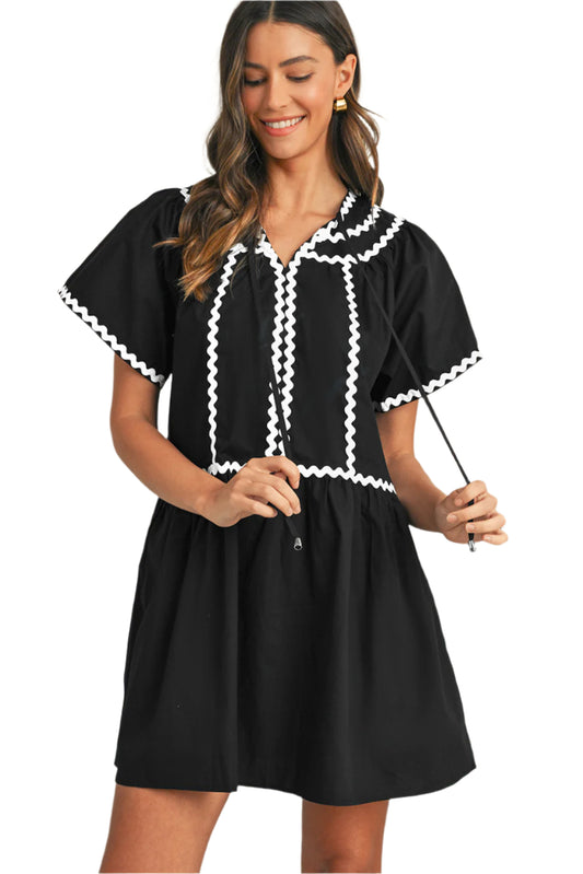 Women wearing a black mini dress with bell sleeves and white ric rac details.