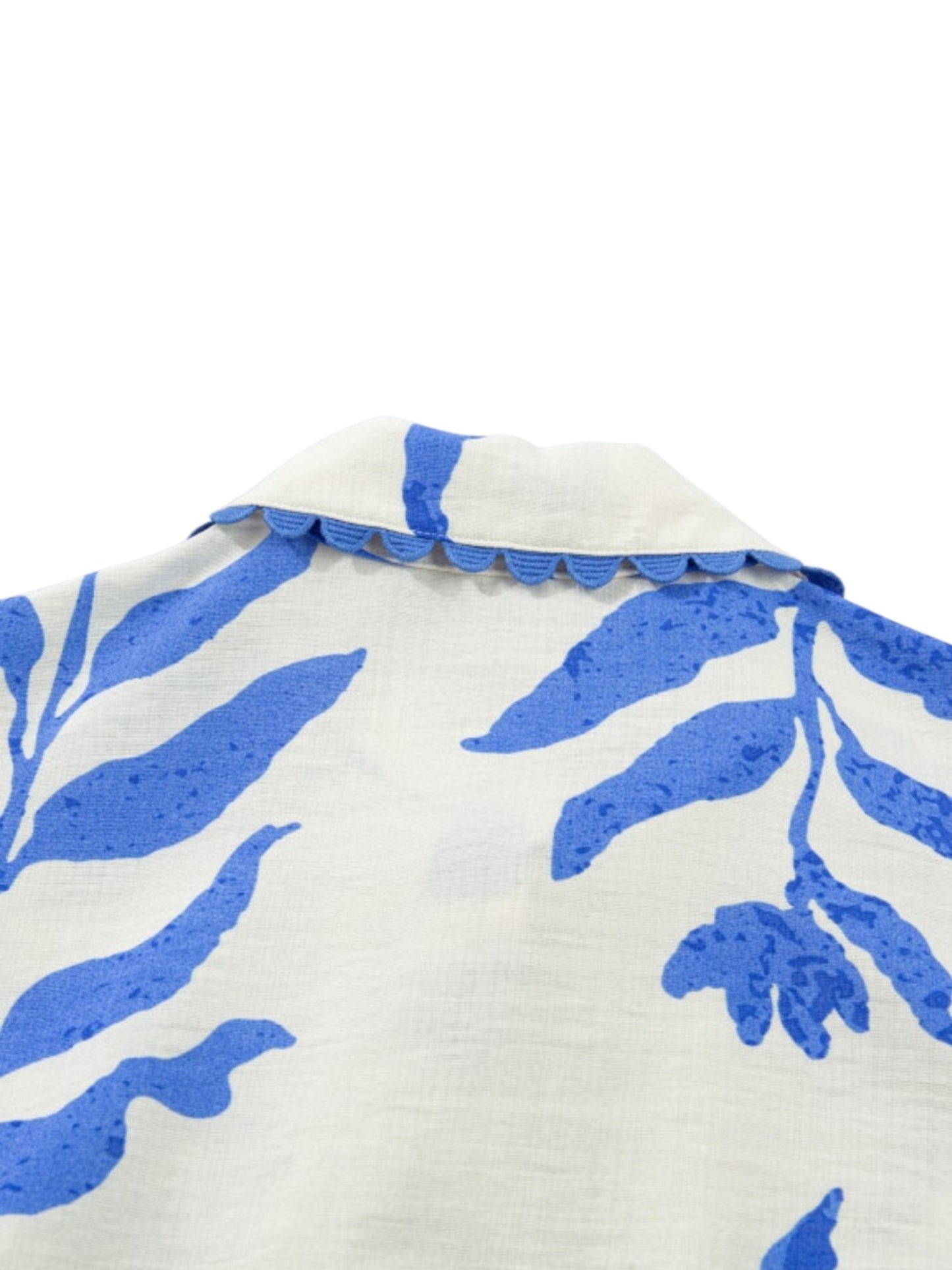 Close-up of a white or off-white fabric with a bold blue botanical leaf pattern and a scalloped blue collar trim, shown against a plain white background.