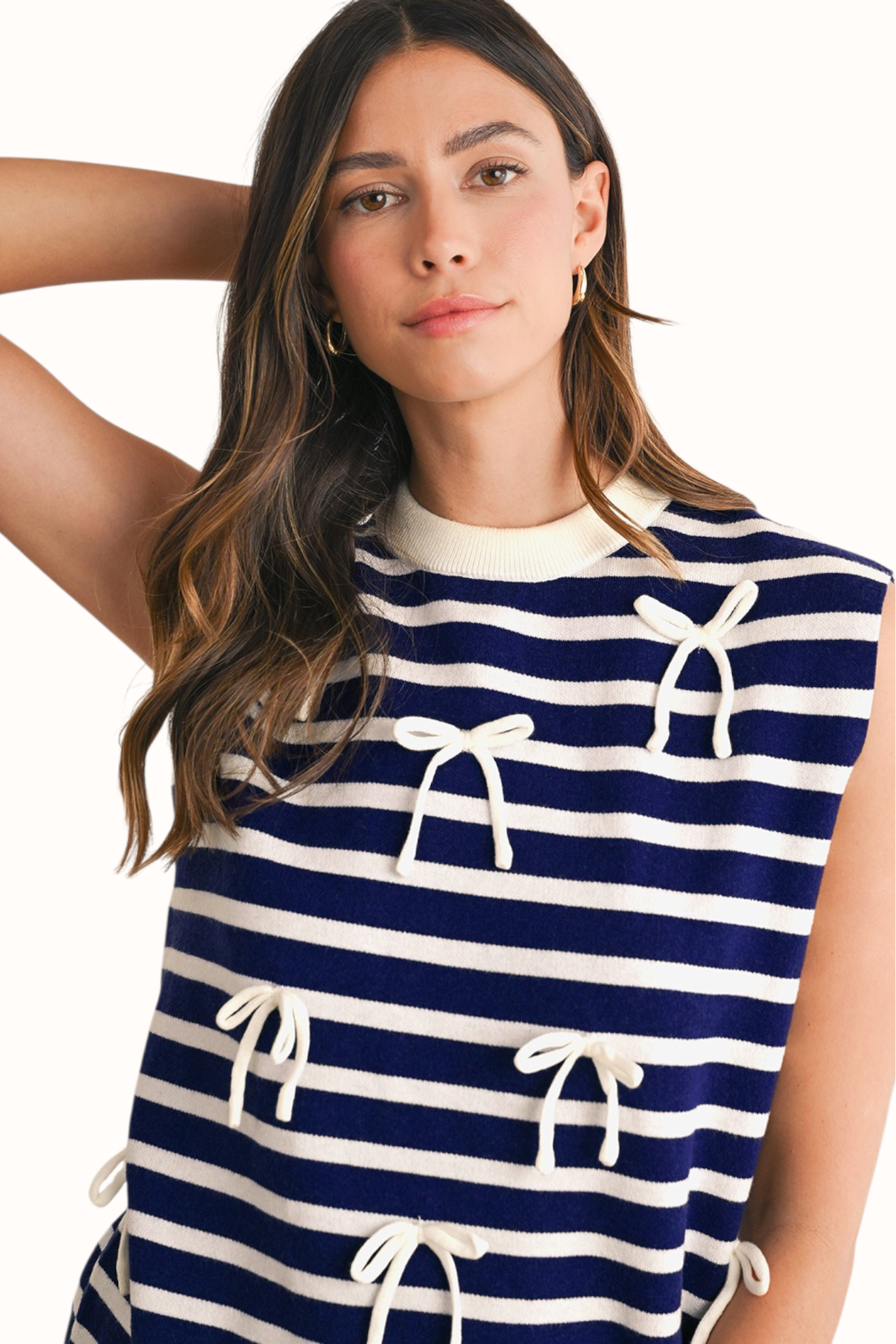 Front view of a navy and white horizontal striped knit vest featuring three delicate white decorative bows and a classic crew neckline.