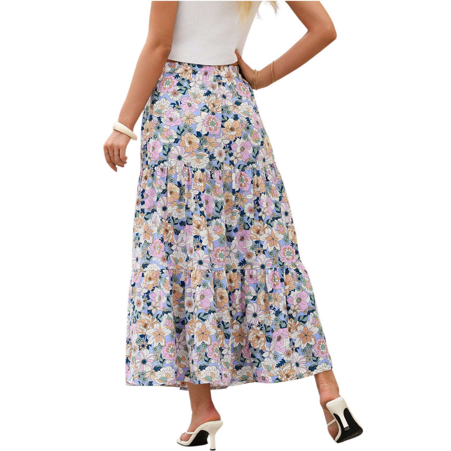 A woman wearing a lightweight, tiered floral maxi skirt in shades of purple and pink with a high side split and elasticated waist. 