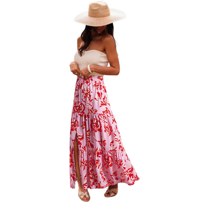 A woman wearing a lightweight, tiered floral maxi skirt in shades of red and pink with a high side split and elasticated waist.