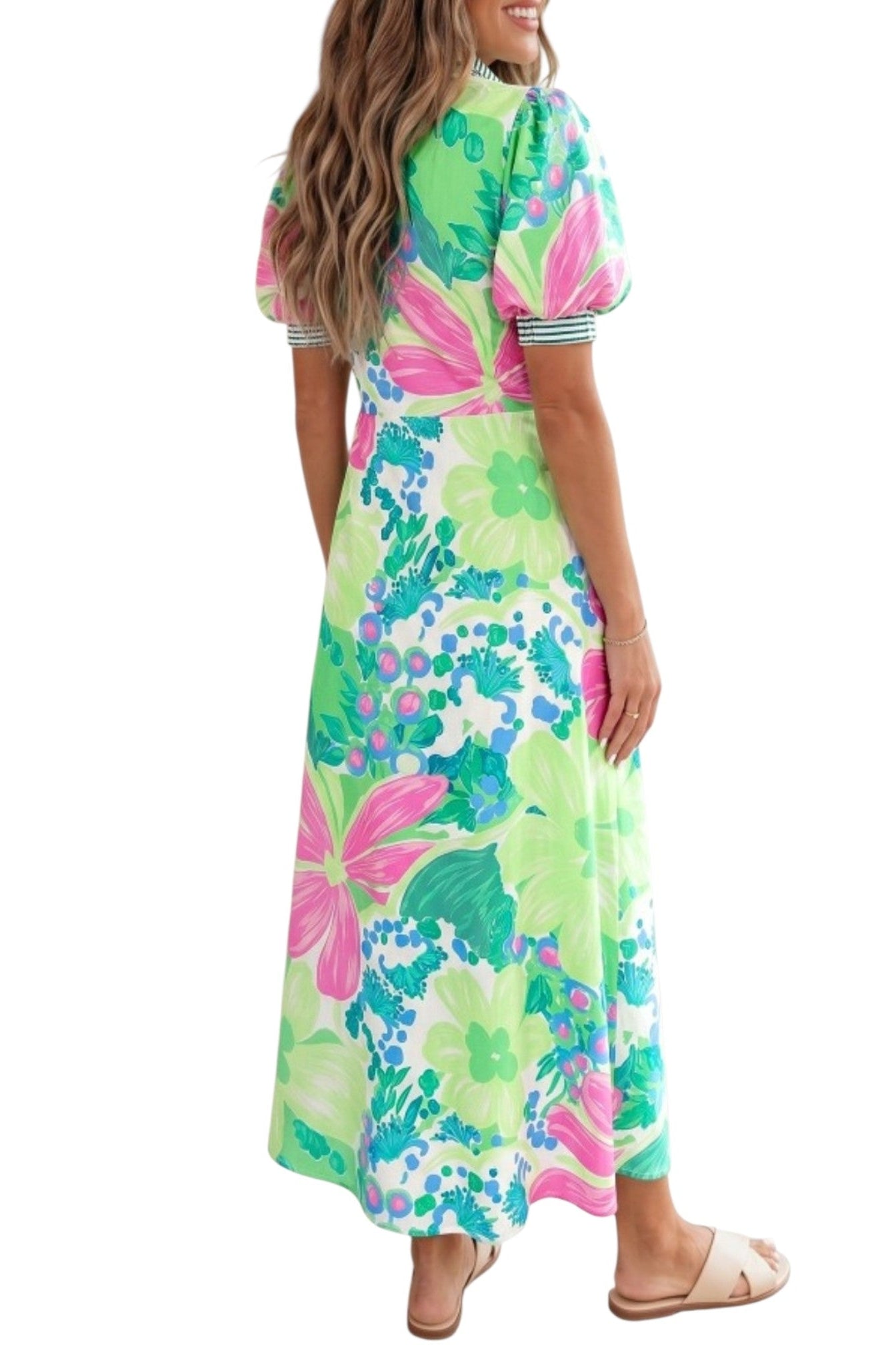 A woman modeling a short-sleeve maxi dress with a vibrant tropical floral print in green, pink, and blue on a white background, shown from a three-quarters back view.