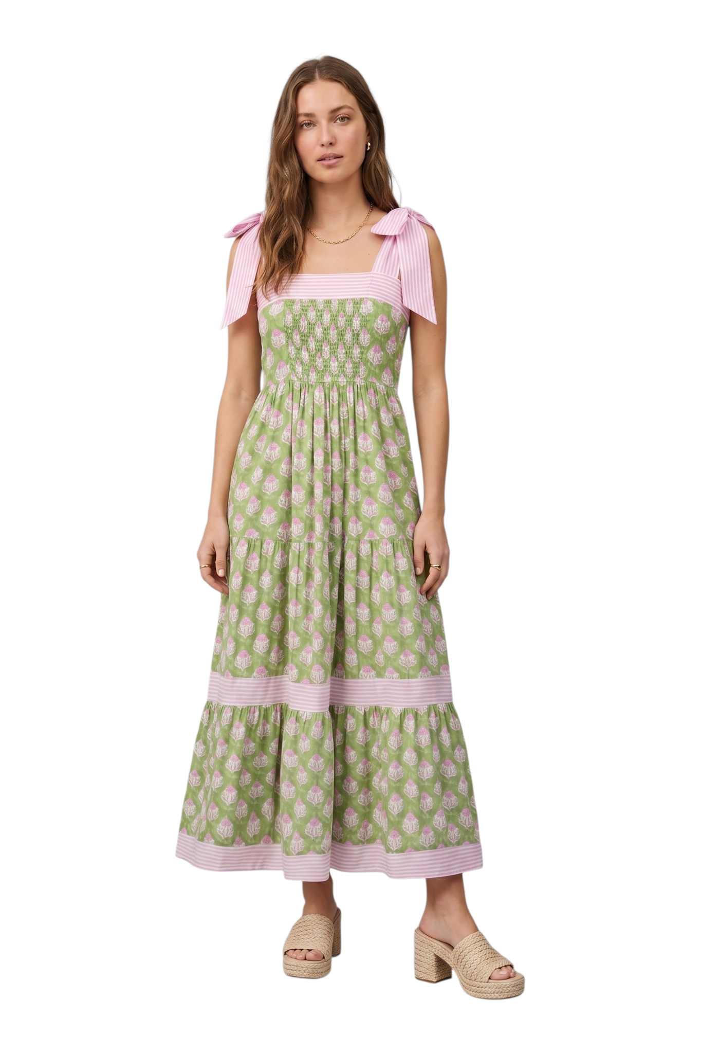 Woman wearing a green and pink botanical block print tiered maxi dress with pink striped tie-knot shoulder straps, smocked bodice, and pink striped hem trim, paired with tan woven platform mule heels, front view