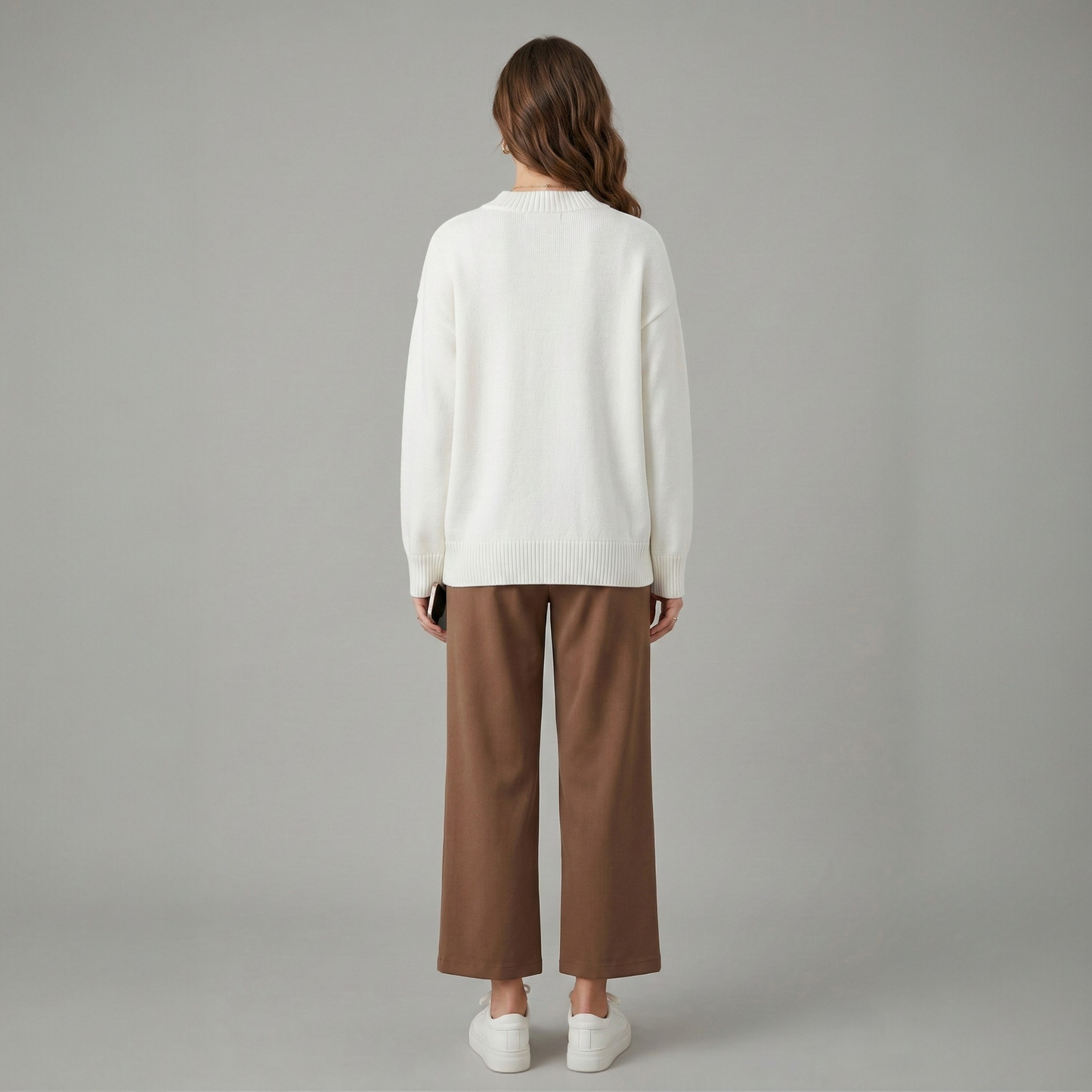 Back view of a model wearing a white knit sweater with a ribbed crew neck, paired with brown trousers.