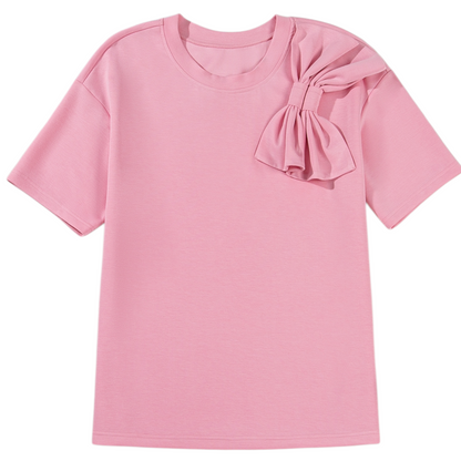 Professional front view of a pink crew neck t-shirt featuring a signature bow detail on the left shoulder and a half-sleeve design.