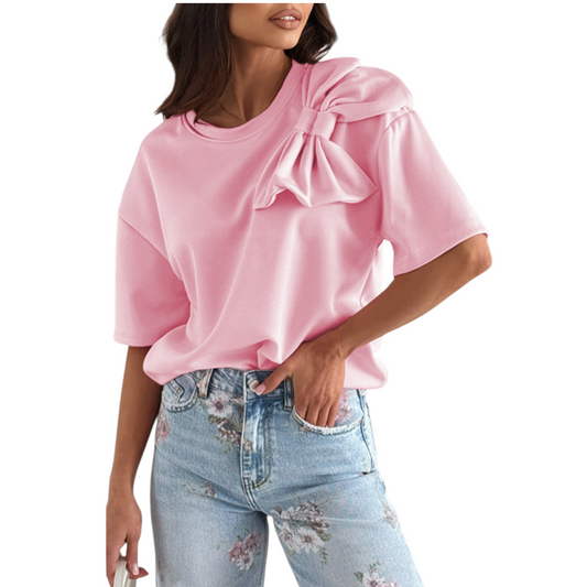 A woman wearing a vibrant pink t-shirt with a large decorative bow applique on the shoulder and relaxed drop sleeves.