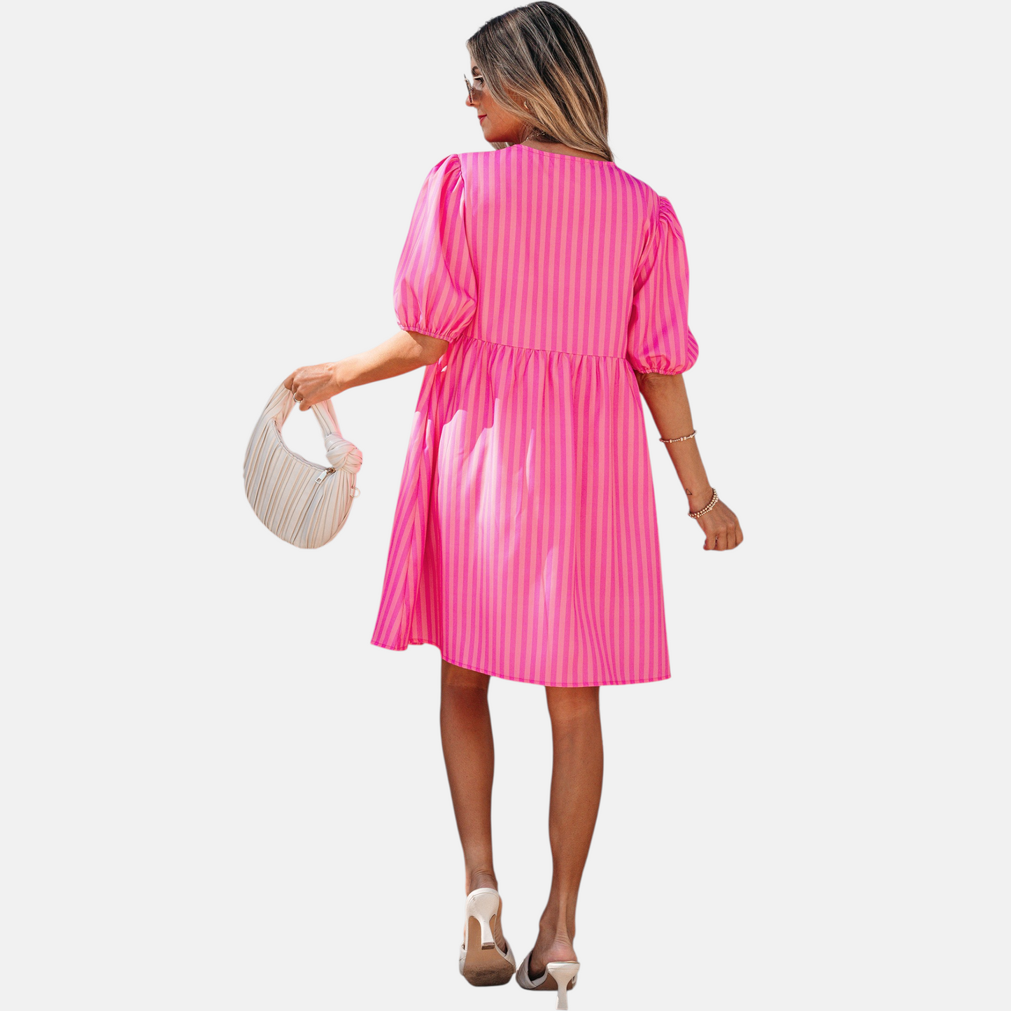 Rear view of a model posing in a vibrant pink striped mini dress featuring puff sleeves, three decorative front bows, and functional side pockets, styled with white slide sandals and a pleated handbag.