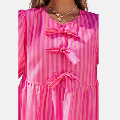Close-up of a pink striped dress with bow details on a white background
