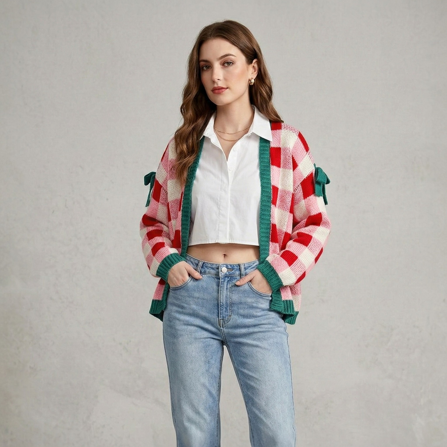 Front view of a model wearing a pink and red checkered open-front knit cardigan with green trim and decorative sleeve bows, styled with a white shirt and blue jeans.