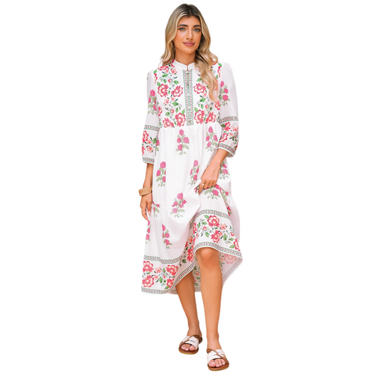 A model wearing a white tiered maxi dress featuring a bright pink floral embroidery design on the bodice and hem, styled with brown sandals.