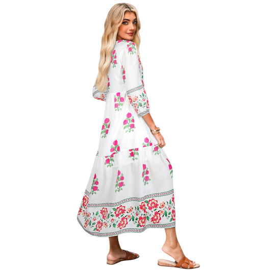A model wearing a white tiered maxi dress featuring a bright pink floral embroidery design on the bodice and hem, styled with brown sandals. Side view.