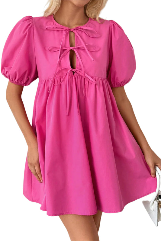 Woman wearing a bright pink puff sleeve mini dress with a tie front design, styled for a chic and playful look, paired with a white clutch.