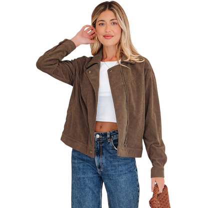 A woman wearing a brown corduroy zip-up jacket over a white crop top and blue jeans, highlighting the gold hardware and functional side pockets.
