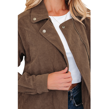 Close-up view of a woman wearing a brown corduroy zip-up jacket over a white crop top and blue jeans, highlighting the gold hardware and functional side pockets.