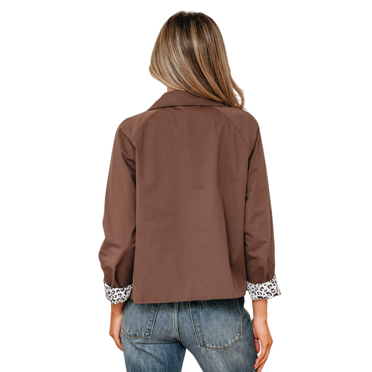 A back view shot of a woman wearing a cropped brown cotton jacket with a classic collar and large tonal buttons, featuring leopard print lining visible at the rolled-up cuffs.