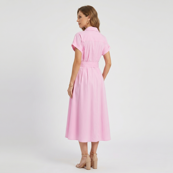 Side profile of  a model wearing a bubblegum pink long shirt dress featuring a collared neckline, short sleeves, and a matching belt with a woven straw buckle.