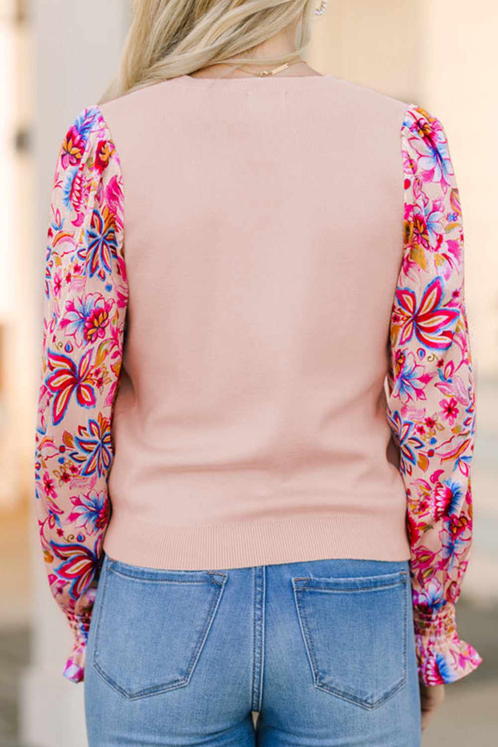 Model standing with back turned in an oatmeal knit top featuring floral print long sleeves.