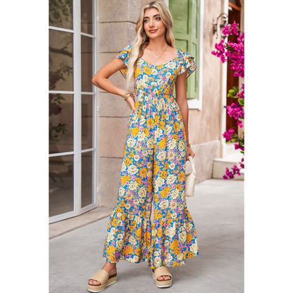 Woman wearing a floral dress standing in front of a building with pink flowers.