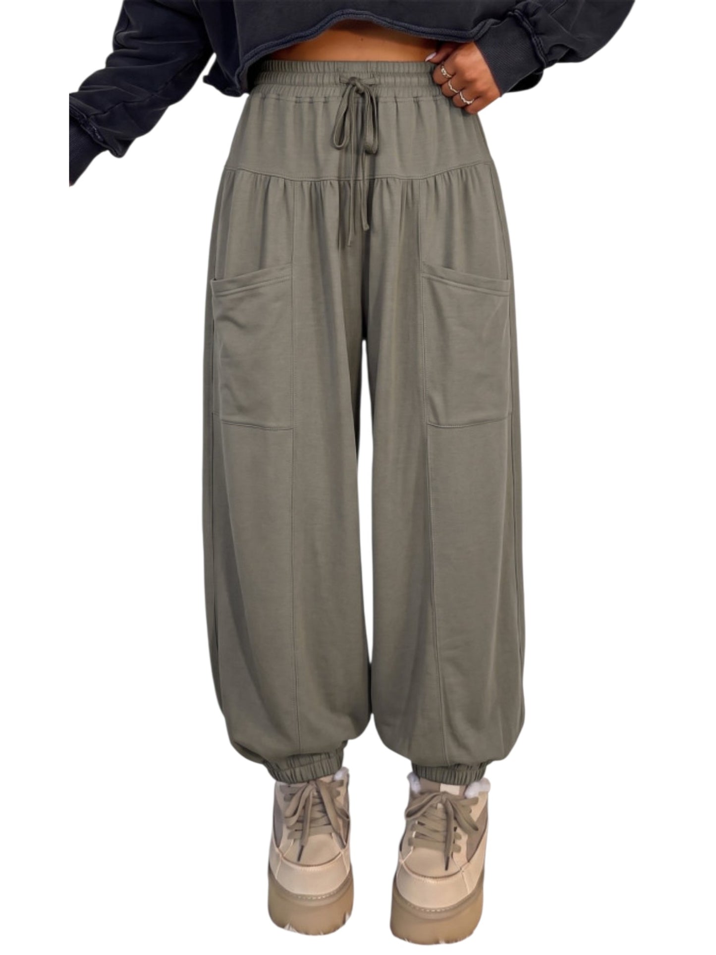 A person wearing loose, high-waisted olive green harem-style pants with an elastic drawstring waist, large front patch pockets, elastic cuffs, and chunky beige platform sneakers against a plain white background.