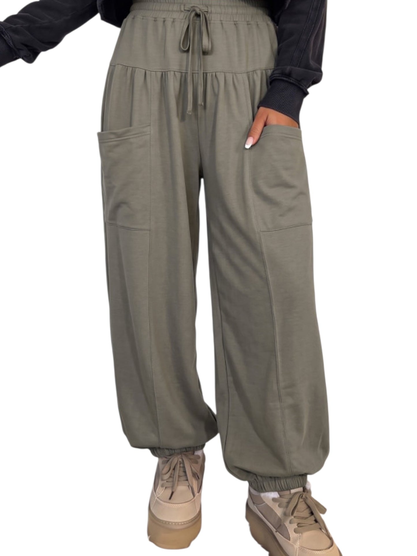 A person wearing loose, wide-leg jogger-style pants in an olive green color, paired with beige sneakers and a black long-sleeve top. The photo is cropped from the chest down against a plain white background.