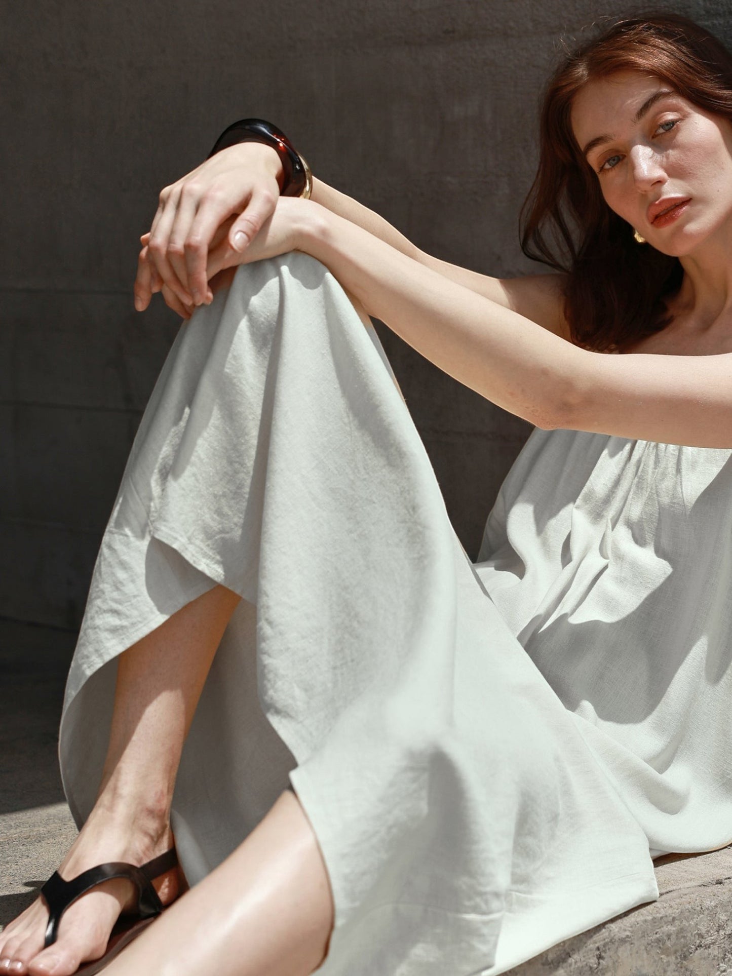 Catherine Martin linen cotton maxi dress in sage green with frayed edges, worn by a woman sitting against a wall.