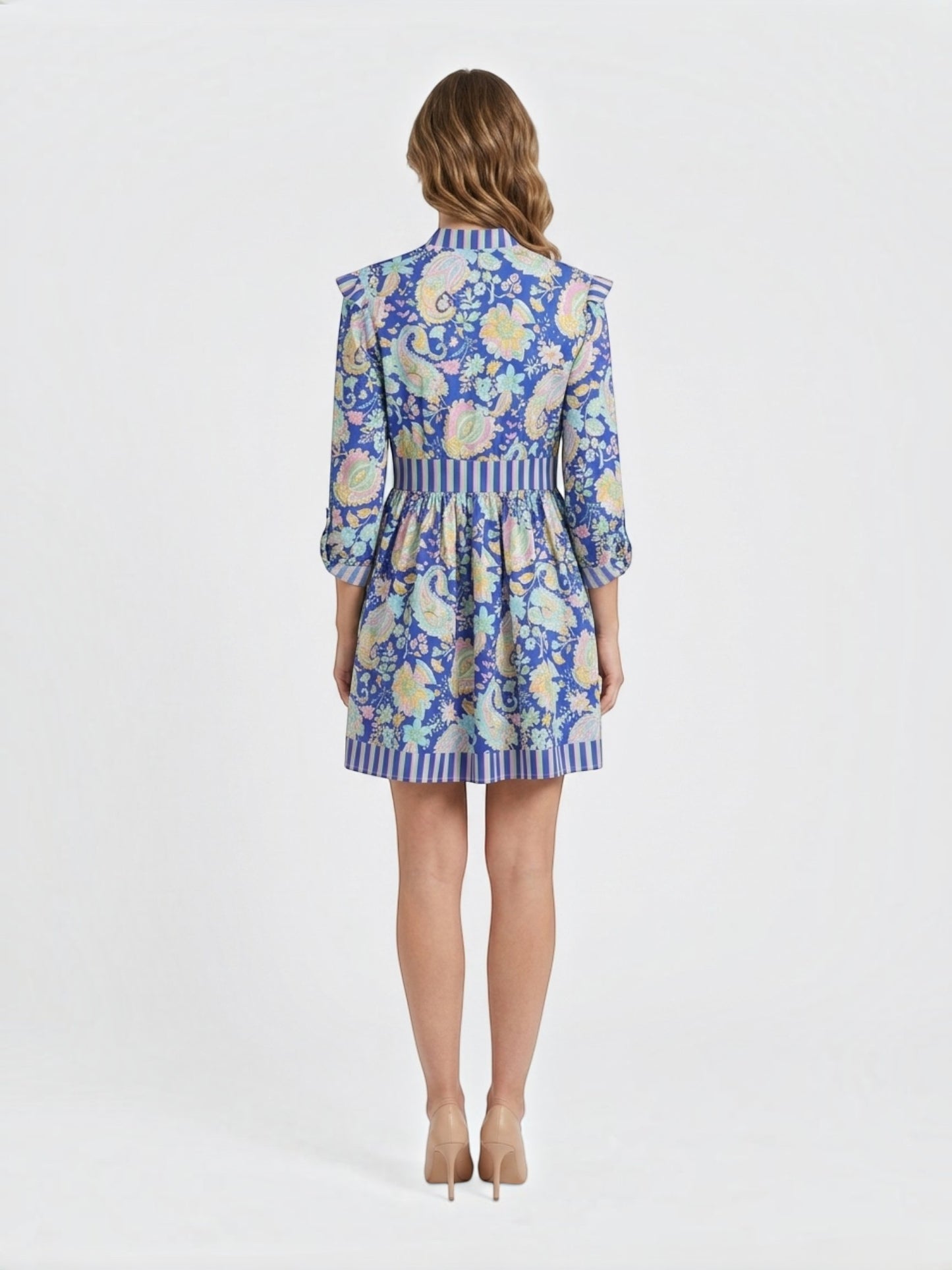 Back view of a Catherine Martin blue paisley print mini dress with ruffled shoulders, button-front, and striped trim on a model