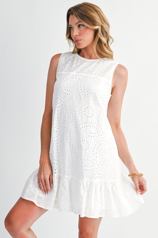 Woman wearing a white dress with eyelet details on a plain background