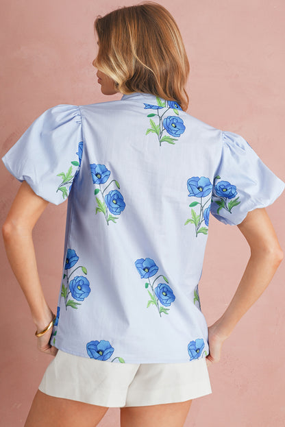 Woman wearing a light blue blouse with floral patterns on a pink background