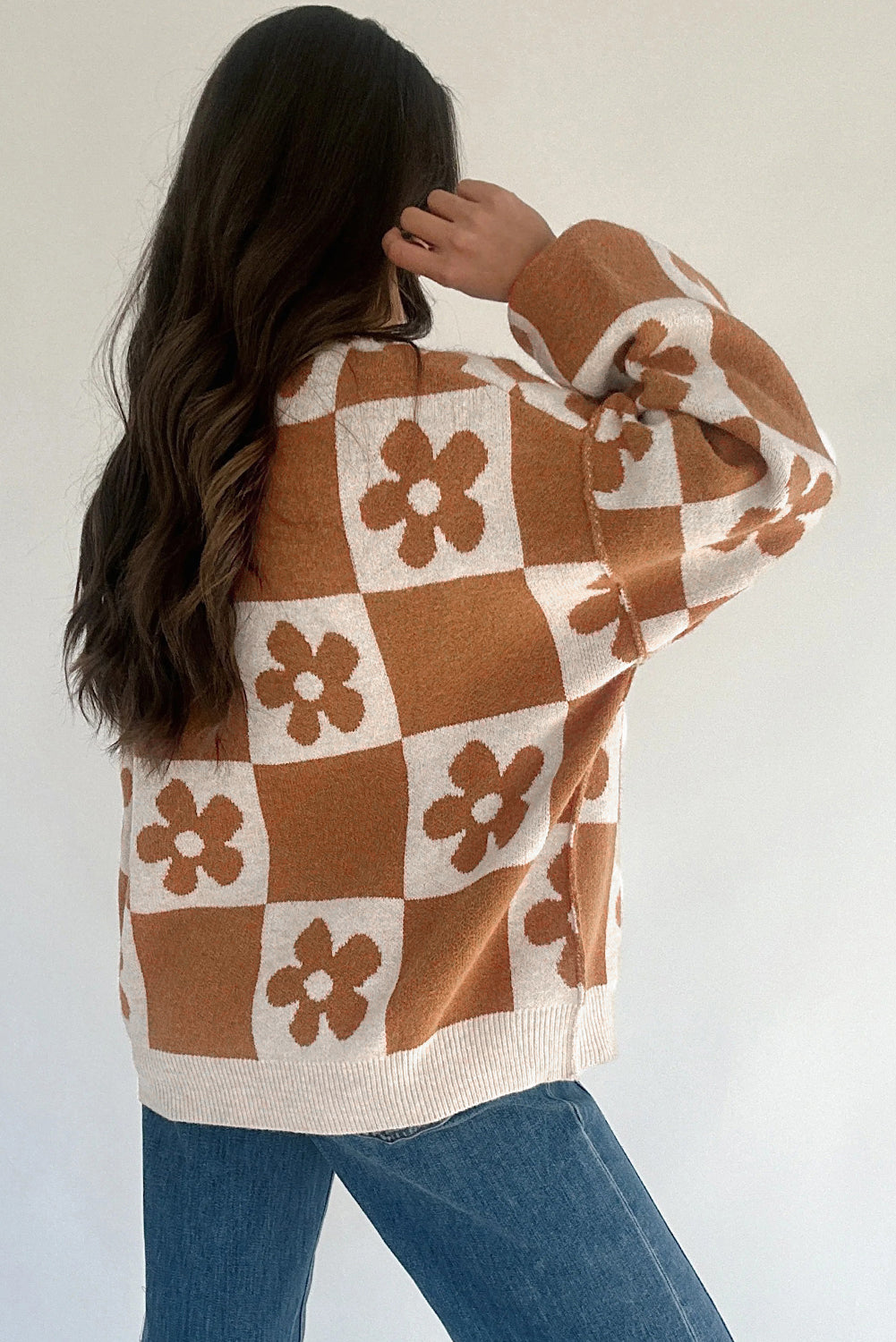 Person wearing a brown and white checkered sweater with floral patterns against a plain background
