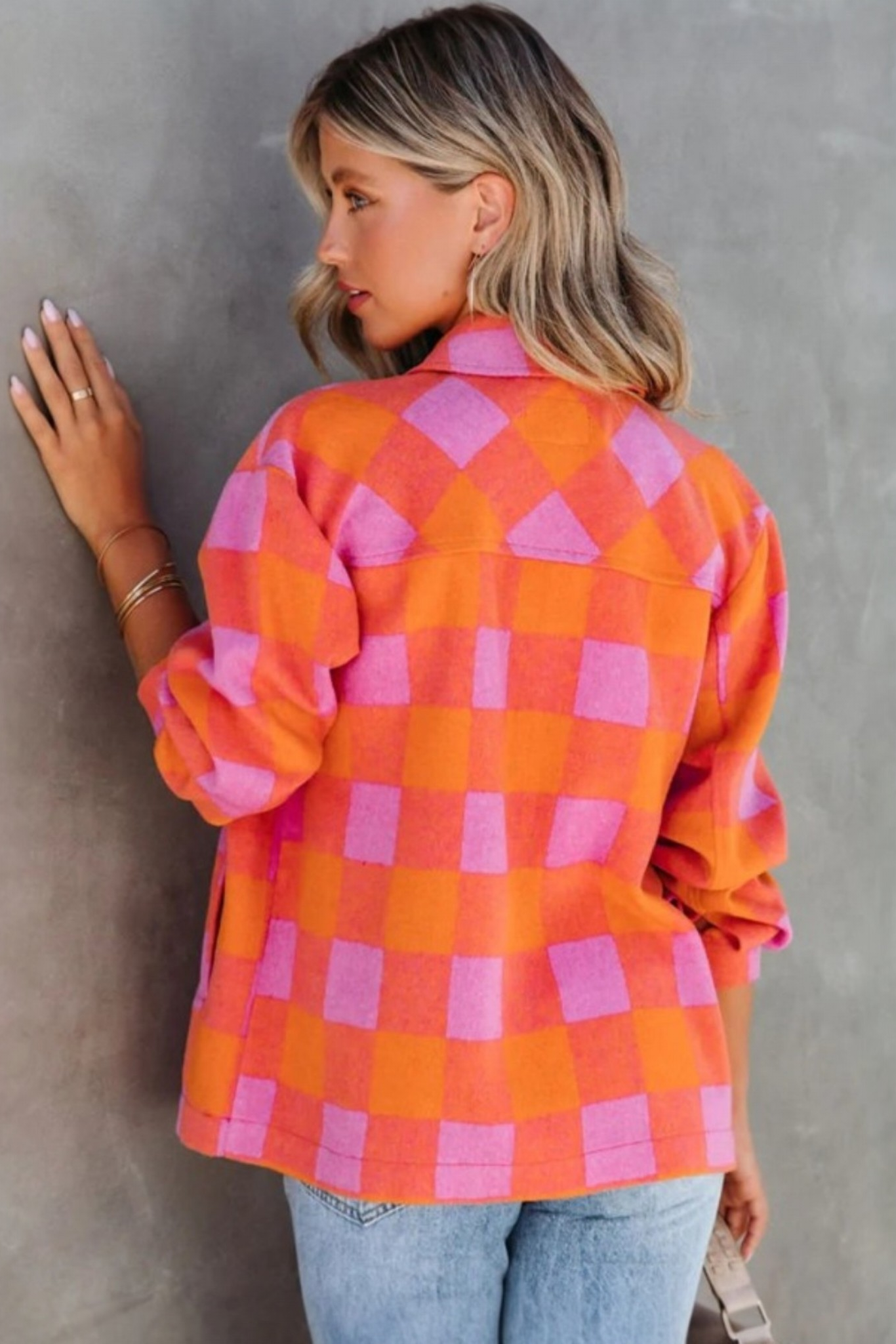 Rear view of a model wearing a pink and orange checkered shacket against a textured wall, highlighting the oversized fit and seamless pattern alignment.