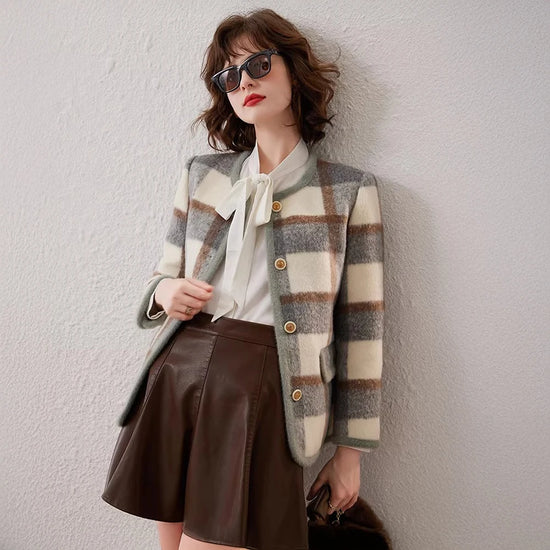 Woman wearing a plaid jacket and brown skirt against a white wall