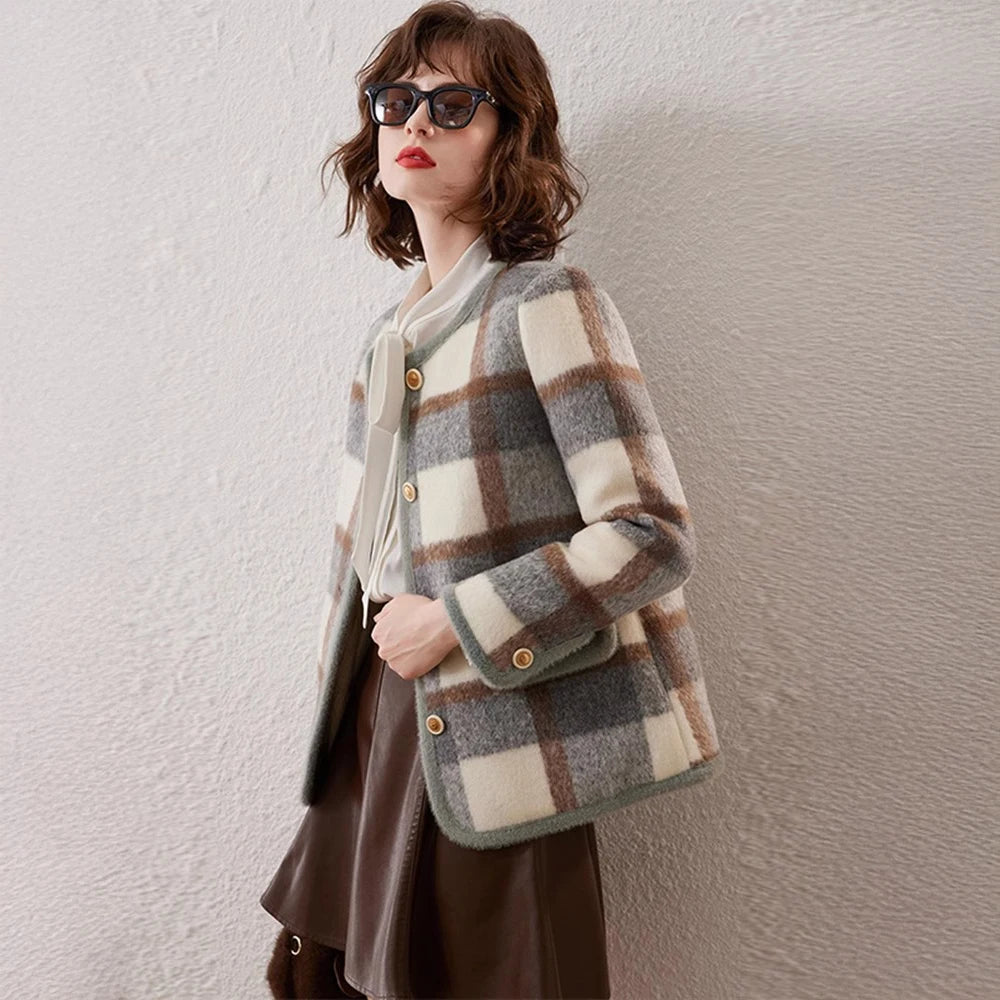 Woman wearing a plaid coat holding a matching bag against a white wall