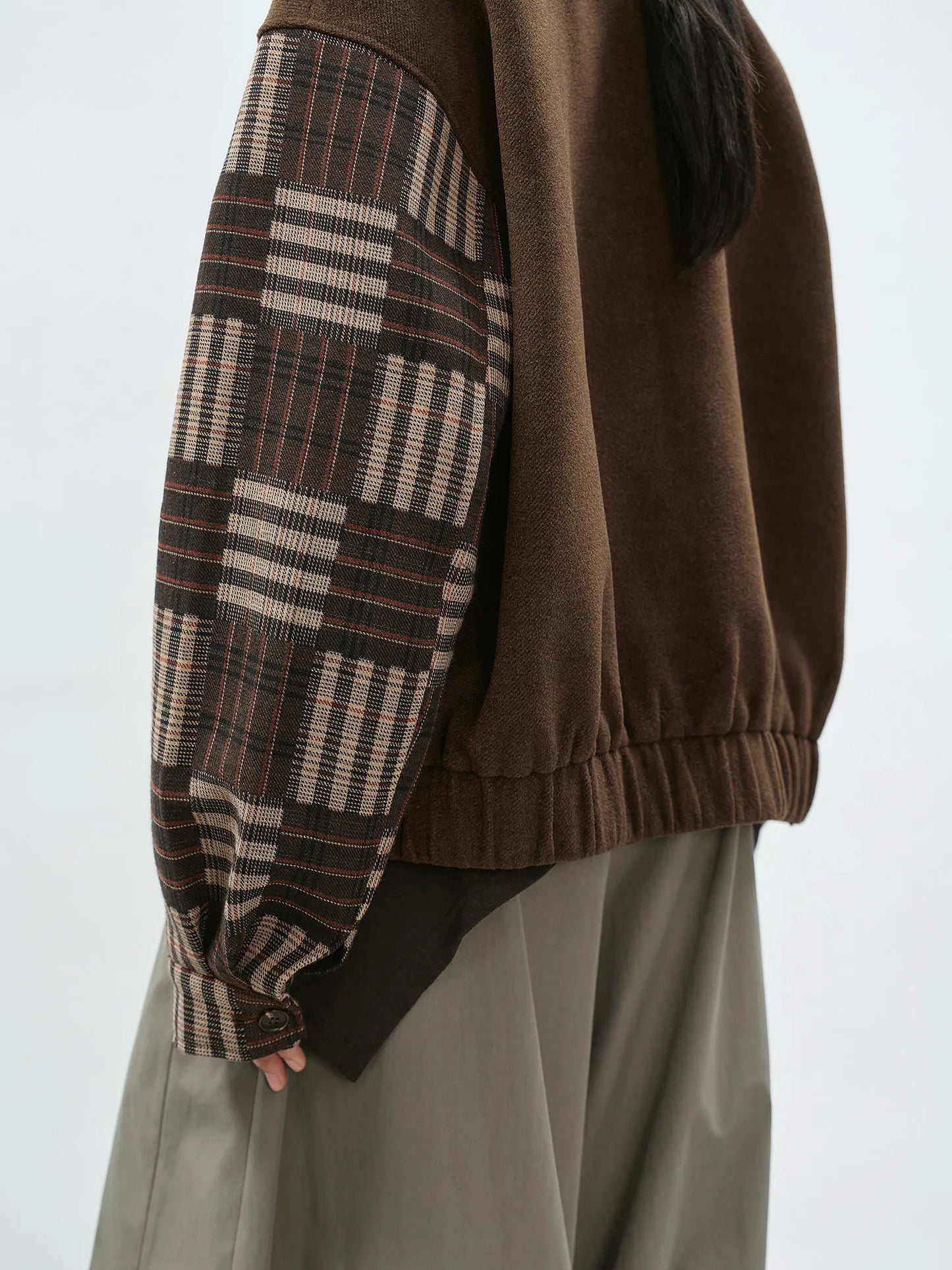 Brown sweater with plaid sleeves worn by a person on a white background