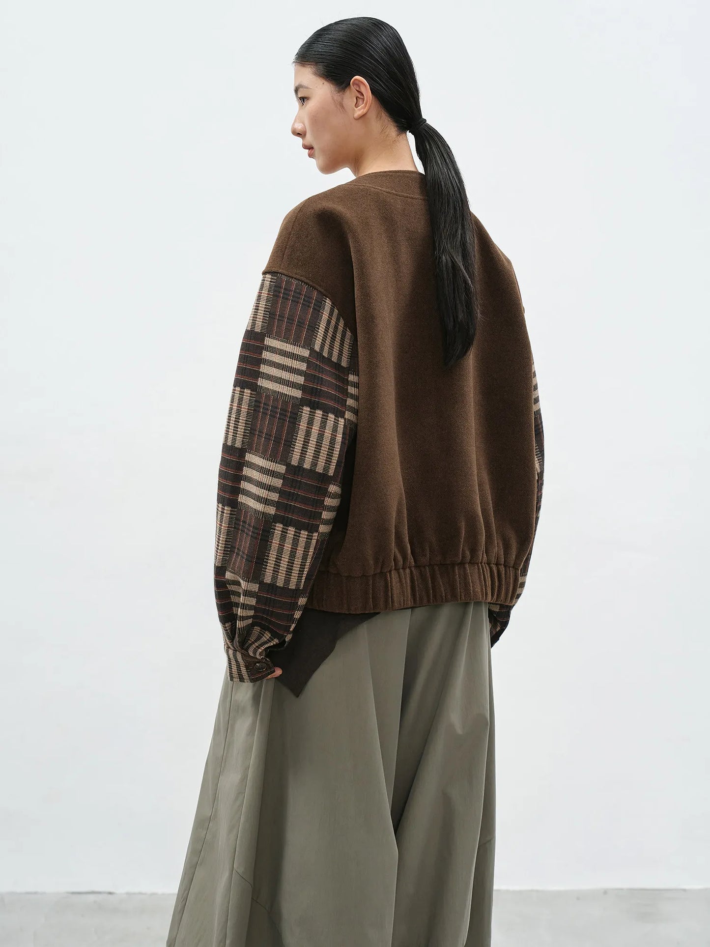 Person wearing a brown sweater with plaid pattern on a white background