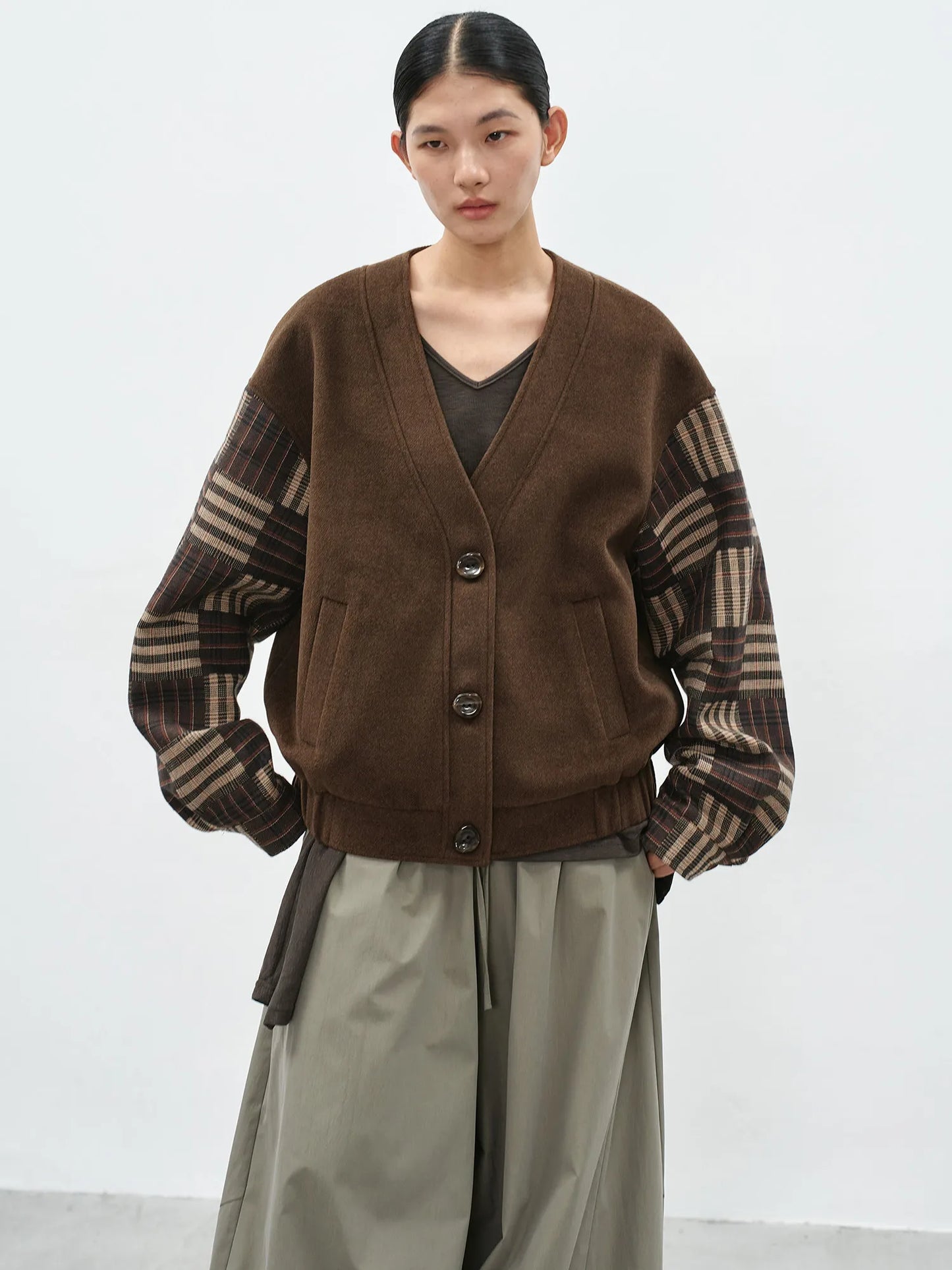 Model wearing a brown v-neck cardigan with contrast checkered sleeves and a loose-fit silhouette for a casual-chic look.