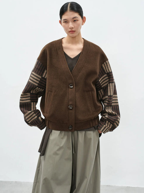 Model wearing a brown v-neck cardigan with contrast checkered sleeves and a loose-fit silhouette for a casual-chic look.