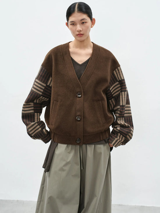 Model wearing a brown v-neck cardigan with contrast checkered sleeves and a loose-fit silhouette for a casual-chic look.
