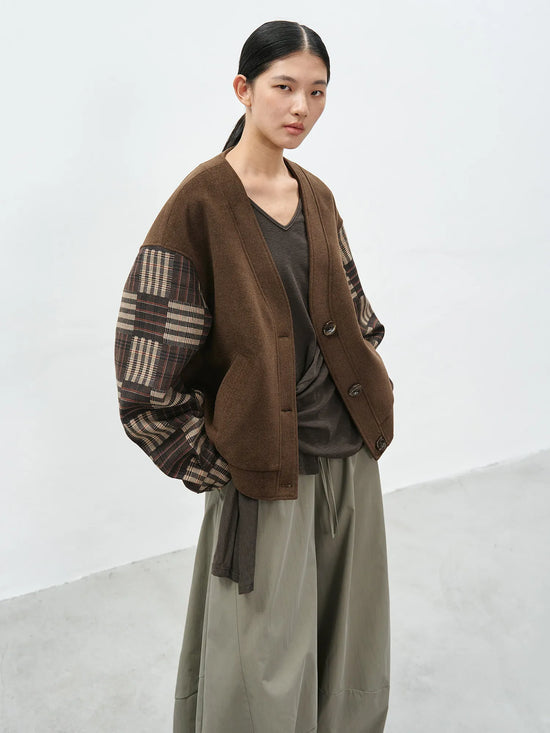 Model wearing a brown v-neck cardigan with contrast checkered sleeves and a loose-fit silhouette for a casual-chic look.