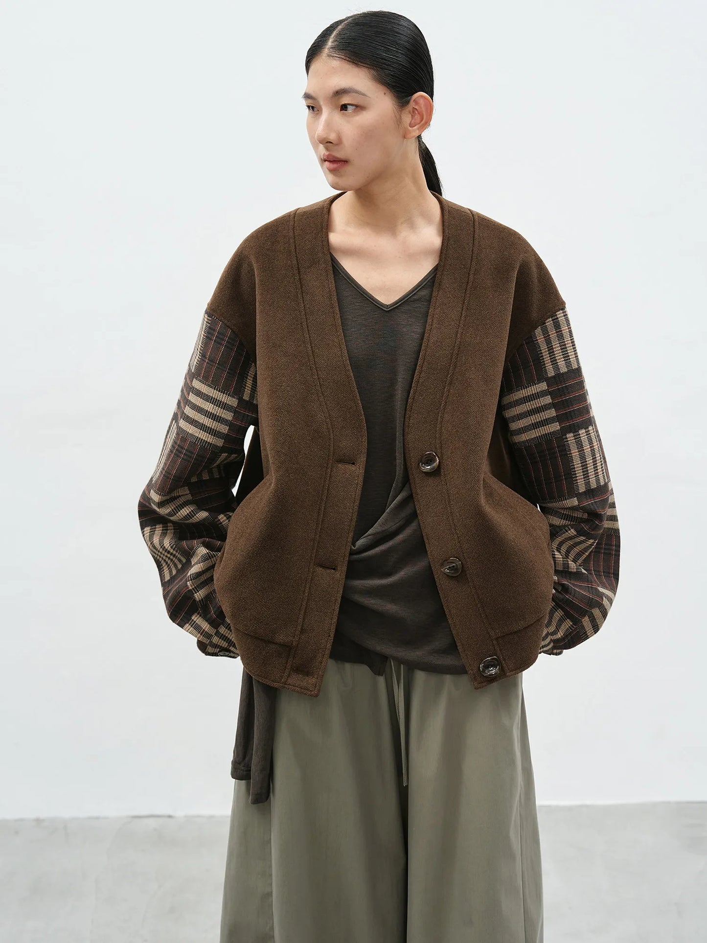 Model wearing a brown v-neck cardigan with contrast checkered sleeves and a loose-fit silhouette for a casual-chic look.