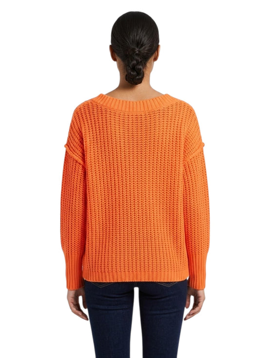 A woman viewed from the back wearing a bright orange textured knit sweater and dark blue jeans against a plain white background.